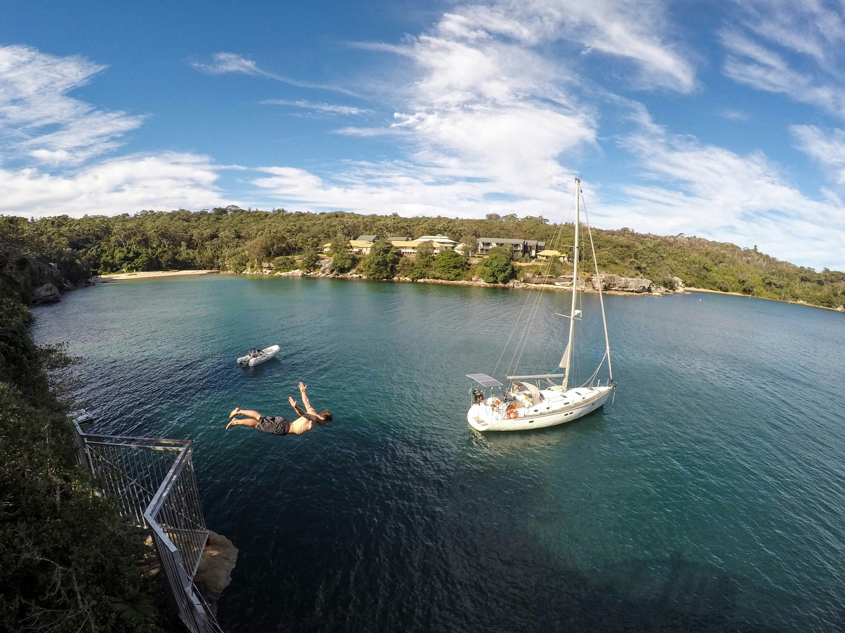 A person diving in front of a sailboat.